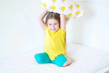 Sevimli küçük kız yatak odasında yatak yastık ile oynarken