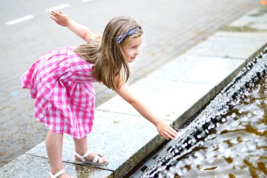 Bir şehir çeşme ile sıcak ve güneşli yaz gününde oynayan sevimli küçük kız