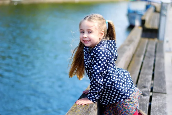Adorabile bambina che gioca vicino a un fiume in un parco soleggiato in una bella giornata estiva — Foto Stock