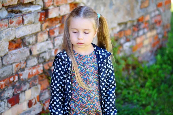 Sad toddler girl standing near brick wall — Stock Photo, Image