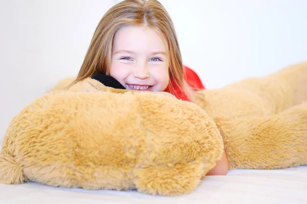 Tatlı küçük kız onu yatakta yatan bir oyuncak ayı sarılma — Stok fotoğraf