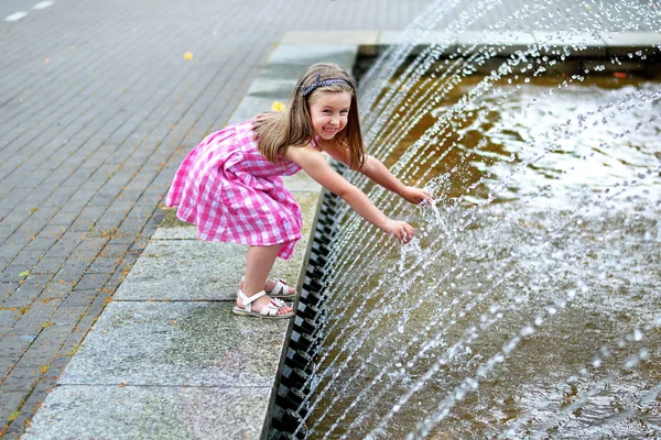 Αξιολάτρευτο κοριτσάκι παίζει με ένα σιντριβάνι της πόλης σε καλοκαιρινή καυτή και ηλιόλουστη μέρα — Φωτογραφία Αρχείου