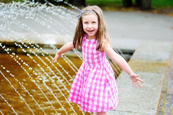 Imádnivaló kis lány játszik a város szökőkút a nap meleg, napos nyár — Stock Fotó