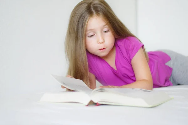 Schattig meisje liggend op het bed en het lezen van een boek — Stockfoto