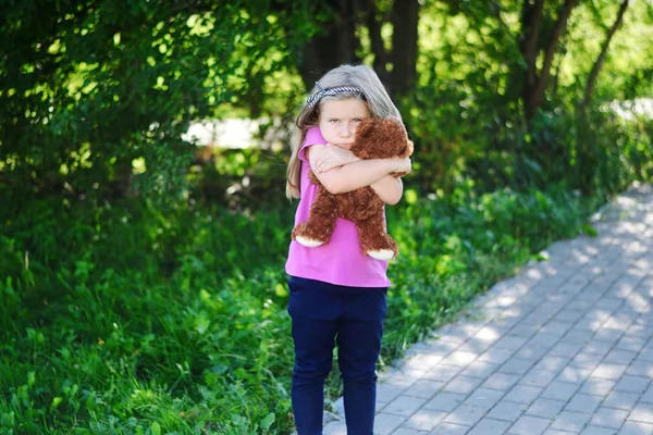Schattig verdrietig meisje met teddybeer in park. — Stockfoto