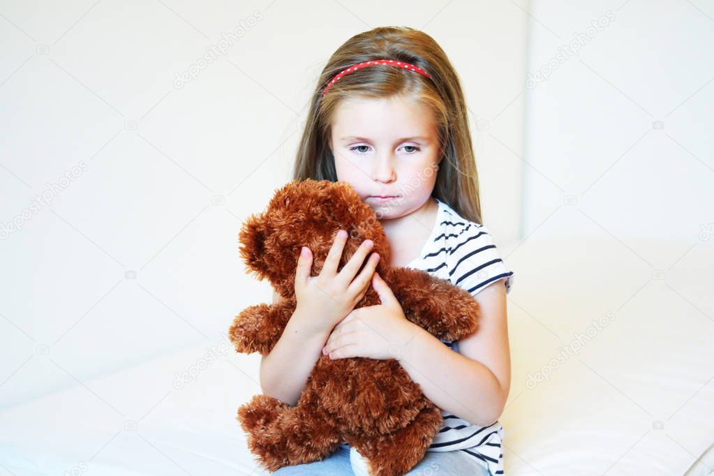 Depressed little girl hugging teddy bear