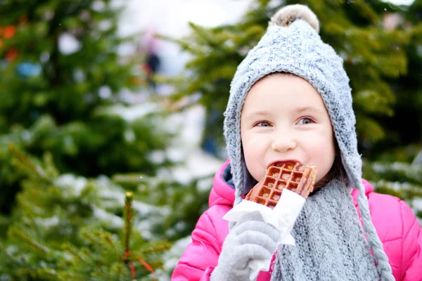 Entzückendes kleines Mädchen isst an kalten Wintertagen warme Waffeln Stockfoto