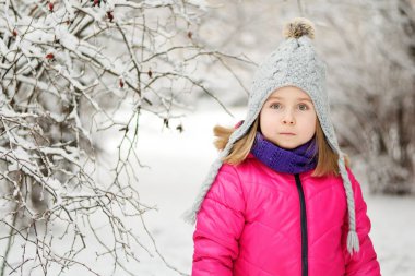 Komik küçük kız kar yağarken güzel kış parkında eğleniyor.