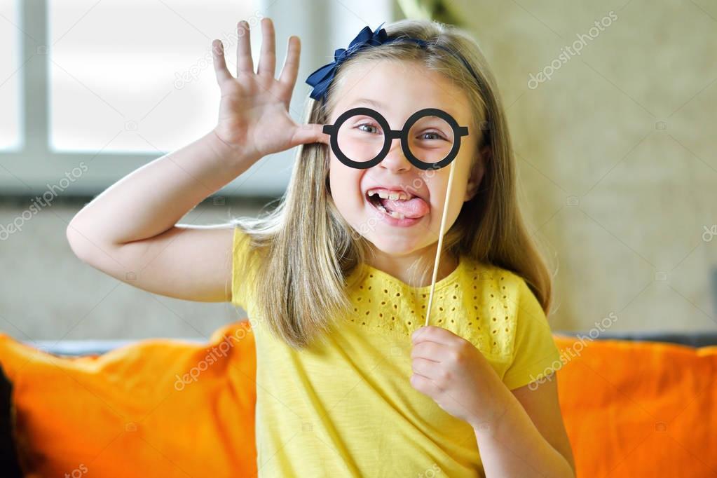 Little girl making face with funny glasses and showing her tongue