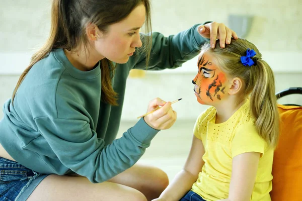 Adorável menina recebendo seu rosto pintado como tigre por artista Fotografia De Stock