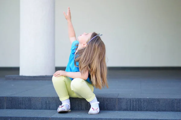 Menina adorável apontar para algo no céu sentado em strairs Fotografia De Stock