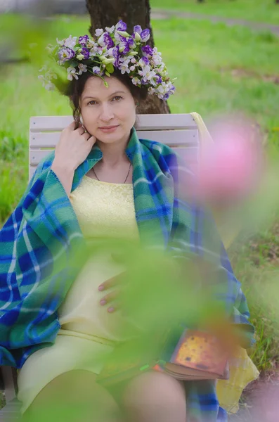 Mooie zwangere vrouw in een gele jurk en een krans van bloemen — Stockfoto