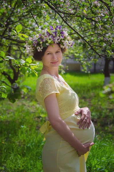 Mujer embarazada bonita en un vestido amarillo y una corona de flores —  Fotos de Stock