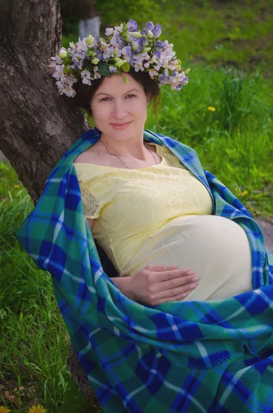 Ganska gravid kvinna i en gul klänning och en krans av blommor — Stockfoto