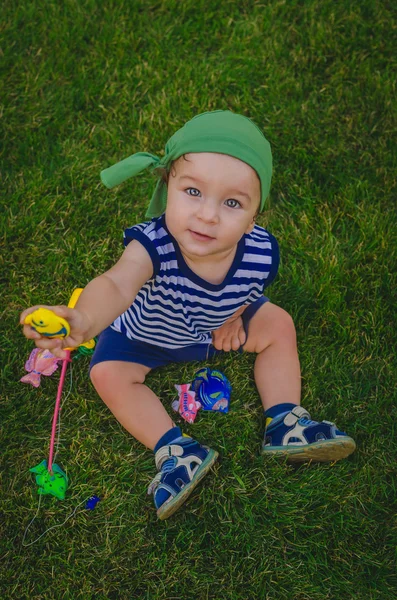 Niño pequeño jugando a los pescadores sentados en una fresca verde la — Foto de Stock