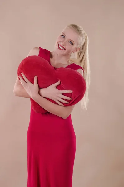 Beautiful young woman in a bright red slinky dress hugging a plu — Stock Photo, Image