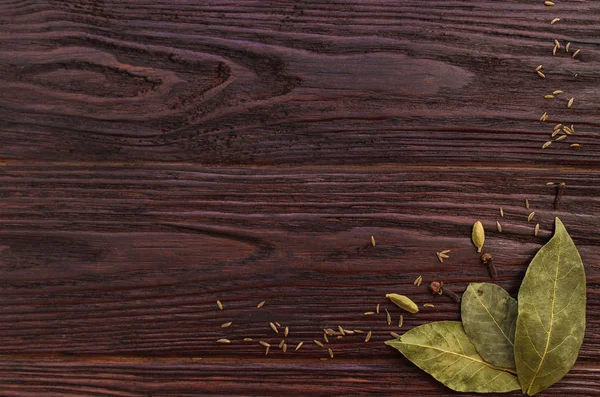 Bay leaves, cloves and caraway seeds on wooden dark textural bac
