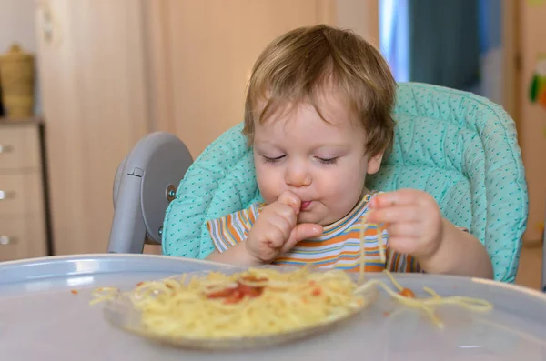 Милый годовалый ребенок ест спагетти в детском кресле . — стоковое фото