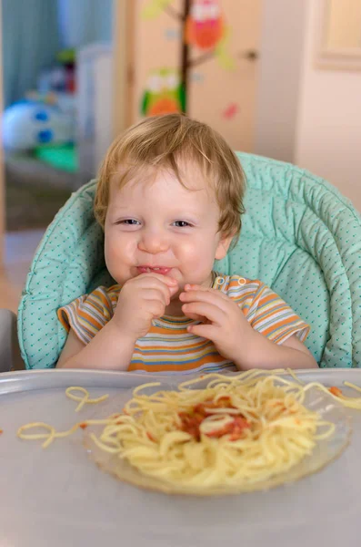 Mignon bébé d'un an mange des spaghettis dans une chaise pour enfants . — Photo