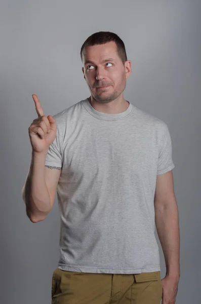 En stilig, muskulös kille i en ljus casual T-shirt på en grå bac — Stockfoto