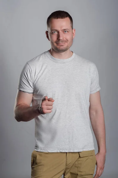 A handsome, muscular guy in a light casual T-shirt on a gray bac — Stock Photo, Image