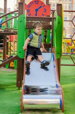 Küçük çocuk parkta slayt (tepe) geliyor. 