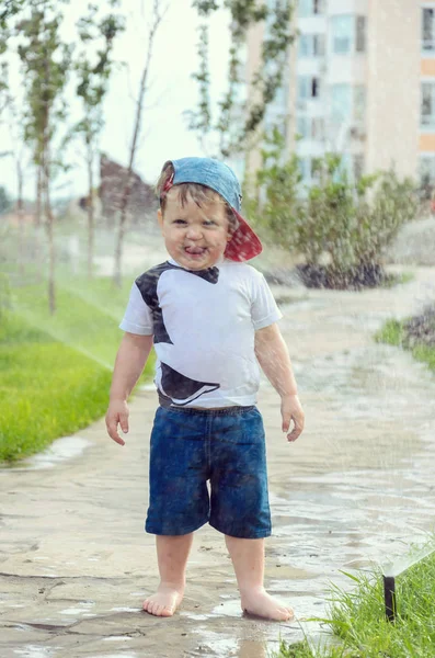 Pequeño niño alegre jugando con césped de riego automático — Foto de Stock