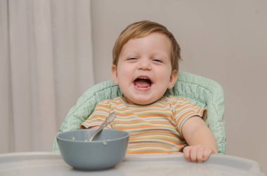 çizgili bir gömlek küçük sarışın çocuk yulaf lapası bir kaşıkla yiyor.