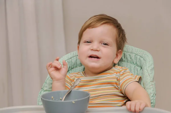 Petit garçon blond dans un T-shirt rayé mange du porridge avec une cuillère — Photo