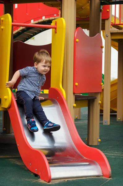 Pequeño niño en una camisa a cuadros, jeans y zapatillas de deporte monta un niño — Foto de Stock