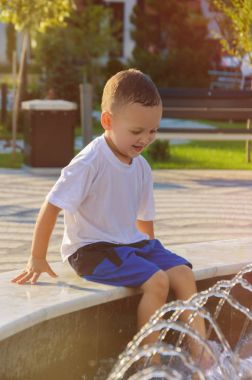 Şort ve tişört vesilesi kenarında oturan küçük çocuk