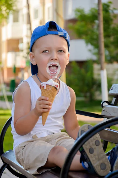 Um rapaz de boné azul e uma t-shirt branca está a comer um gelado. — Fotografia de Stock