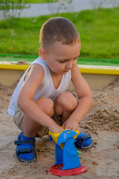 Niño en camiseta blanca excavando con entusiasmo en una caja de arena — Foto de Stock