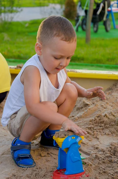 Niño en camiseta blanca excavando con entusiasmo en una caja de arena — Foto de Stock