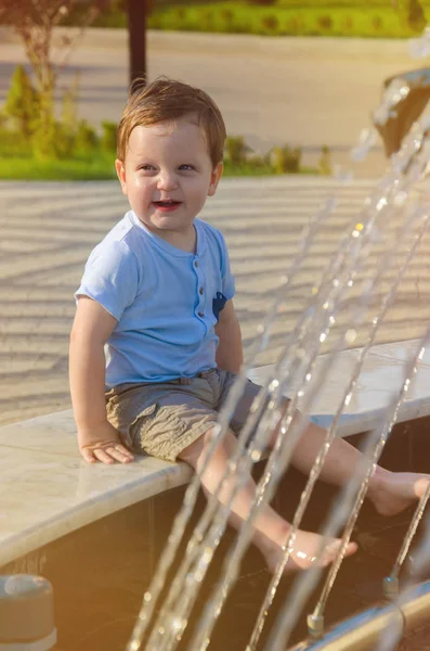 Niño pequeño en pantalones cortos y camiseta sentado en el borde del foun — Foto de Stock