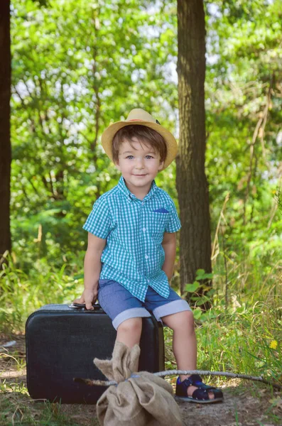 Niño con camisa a cuadros y sombrero de paja sentado en una suitcas — Foto de Stock