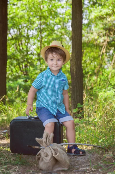 Niño con camisa a cuadros y sombrero de paja sentado en una suitcas — Foto de Stock