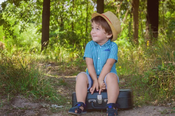 Niño con camisa a cuadros y sombrero de paja sentado en una suitcas — Foto de Stock