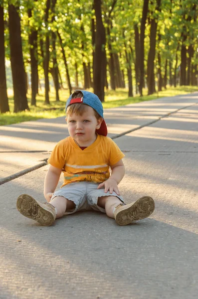 Triste niño se sienta en medio de la carretera en el parque — Foto de Stock