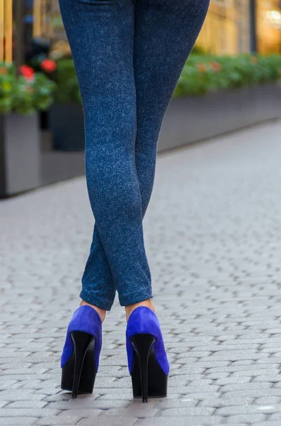 Hermosas piernas delgadas femeninas en jeans ajustados y zapatos azules en un — Foto de Stock