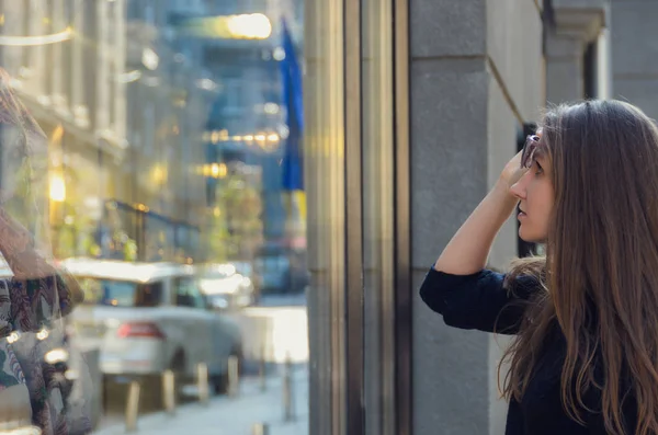 Hermosa chica levanta sus gafas de sol y mira el escaparate o — Foto de Stock