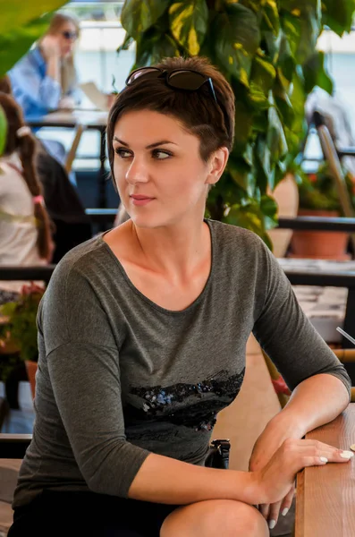 Beautiful woman with short hairdo sits on a summer terrace at a — Stock Photo, Image