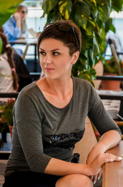 Mulher bonita com penteado curto senta-se em um terraço de verão em um — Fotografia de Stock