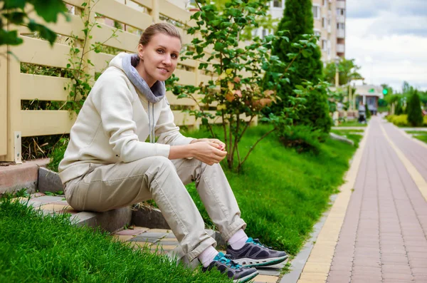 Slanke vrouw in een beige sport pak zit op de trappen van haar po — Stockfoto