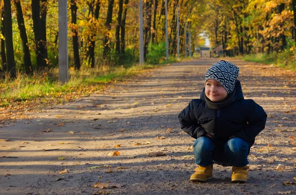 Encantador niño de dos años en una chaqueta azul y un sombrero abigarrado sentado — Foto de Stock