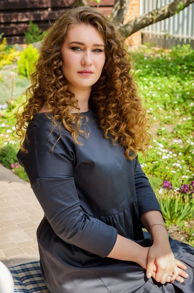 Mulher encantadora com cabelo encaracolado chique descansando no quintal de sua — Fotografia de Stock