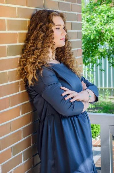 Pěkná žena s elegantní kudrnaté vlasy stojí u zdi v — Stock fotografie