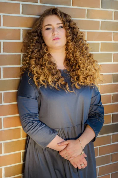 Nice woman with chic curly hair stands near a brick wall in the — Stock Photo, Image