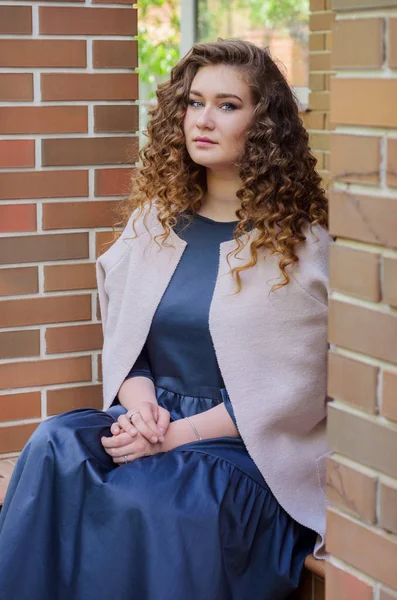 Nice woman with chic curly hair in a long gray dress and a light — Stock Photo, Image