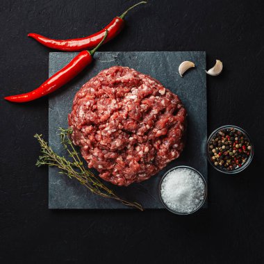 Siyah zemin üzerinde baharatlı köfteler (biber, tuz) için taze doğranmış et yığını. Et yemekleri hazırlamak için gerekli malzemeler.